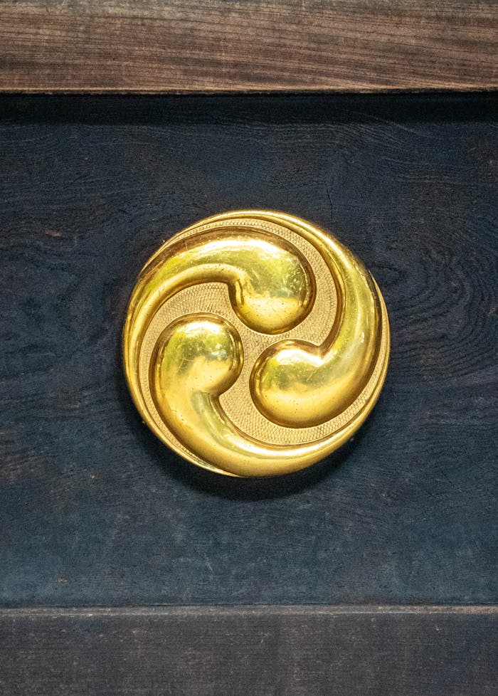 About Us A shiny golden triskelion symbol prominently displayed on a dark wooden backdrop